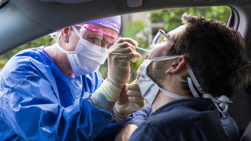 Jemand wird im Auto sitzend mit einem Tupfer durch eine Rachenprobe auf das Coronavirus getestet.