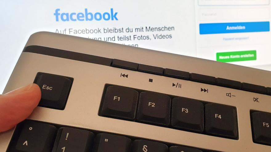 Daumen auf ESC-Taste einer Tastatur vor dem Login-Bildschirm von Facebook
