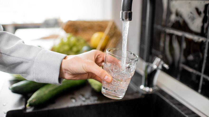 Jemand lässt am Waschbecken Wasser in ein Glas laufen.