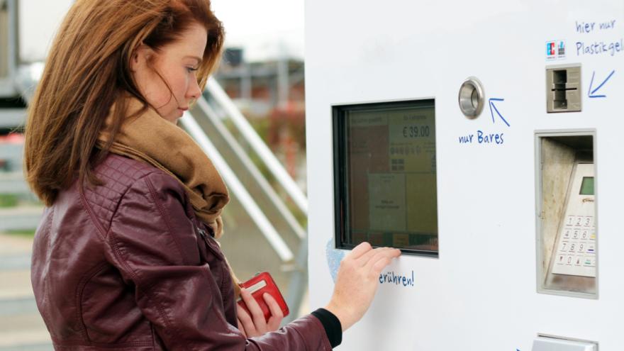 Eine junge Frau sucht ein passendes Ticket am Fahrkartenautomat.