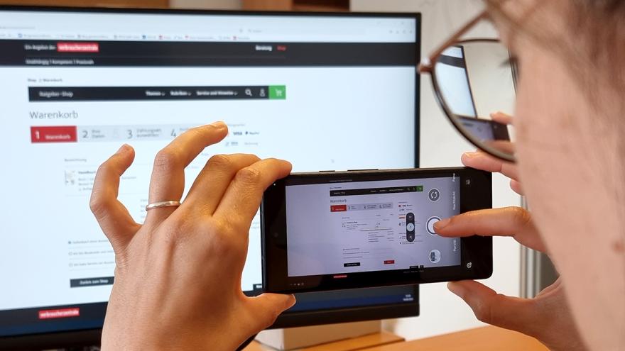 Eine Frau richtet Smartphone auf einen Monitor, um ihn zu fotografieren