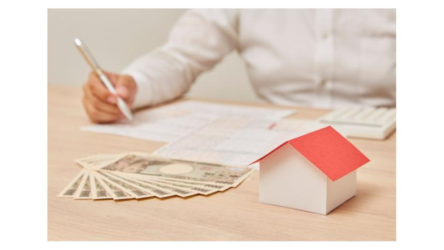 Papierhaus, Geld,  Unterlagen, eine männliche Hand mit Kugelschreiber