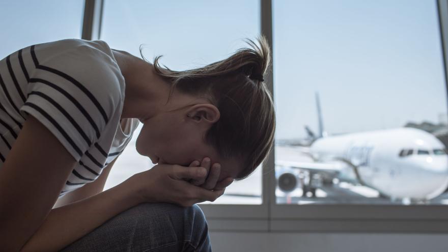 eine Frau mit den Kopf auf den Knie (traurig) im Hintergrund ein Flugzeug