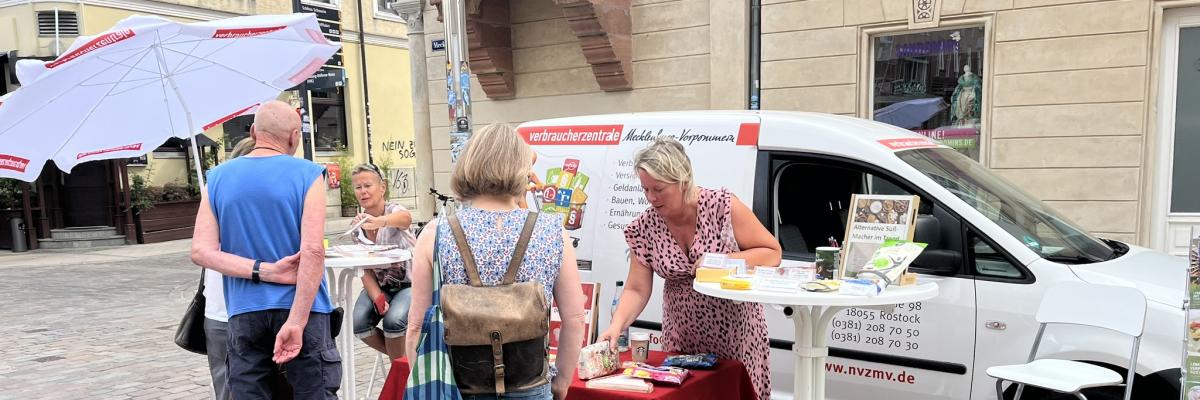 das Auto der Verbraucherzentrale mit einem Infostand davor, vor dem stand stehen Menschen