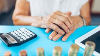 Eine Senioren sitzt mit einem Taschenrechner am Tisch und zählt Münzen