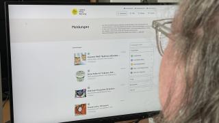 Person schaut auf einen Bildschirm, auf dem die Internetseite lebensmittelwarnung.de aufgerufen ist