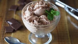 Ein Glasbecher mit Schokoeiskugeln, ein Löffel und Schokoladenstückchen