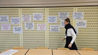 Eine june Frau geht an einer Pinwand vorbei, an der viele Zettel angepinnt sind