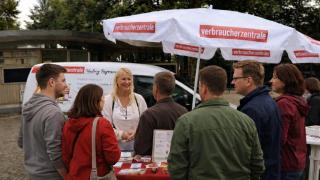 Stand im Freien (Baüme im Hintergrund) mit einem Verbraucherzentralen Schirm