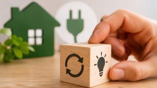 Hand mit einem Holzwürfel / Hintergrund Papierschnitt ein Haus und Stecker